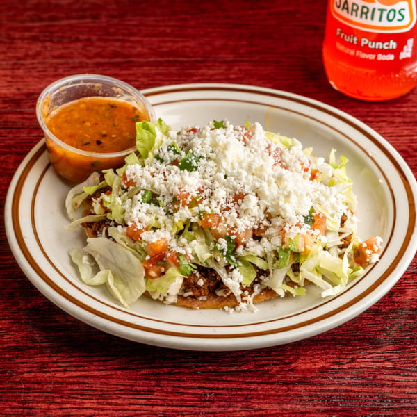 A Nally's Kitchen Mexican tostada with meat, lettuce, tomatoes, and cheese, with a side of salsa.