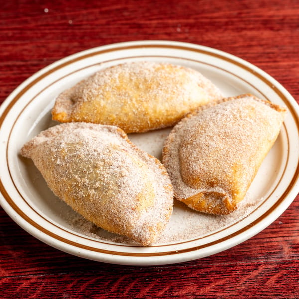 Three golden-brown Nally's Kitchen empanadas, coated in cinnamon sugar, on a white plate.
