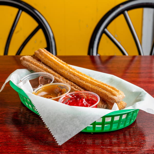 Nally's Kitchen churros in a green basket with chocolate, caramel, and strawberry dipping sauces.