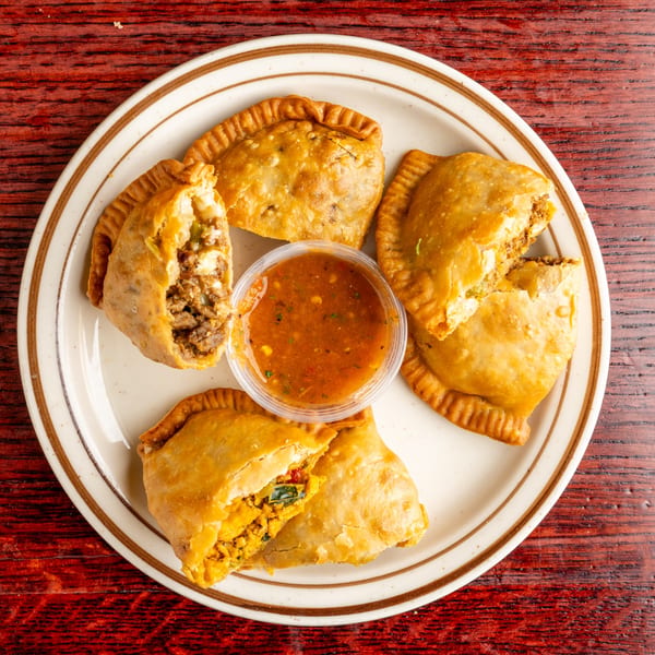 Four golden-brown Nally's Kitchen empanadas, two cut open to show savory fillings, with a side of salsa.