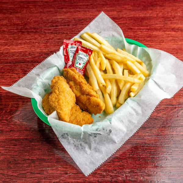 Chicken tenders and french fries with two ketchup packets in a green basket on a wooden table.