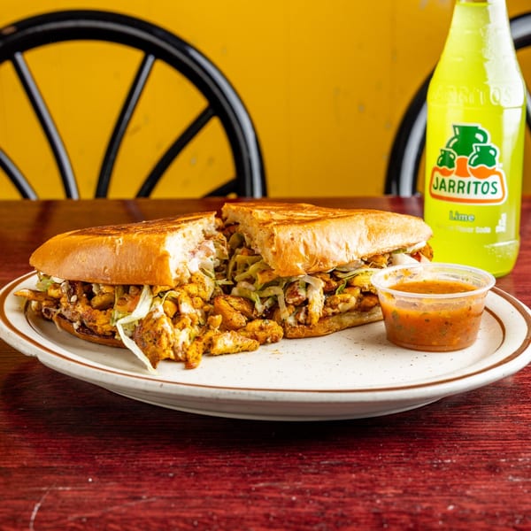 A Nally's Kitchen Mexican torta, cut in half, with a side of salsa and a Jarritos soda.
